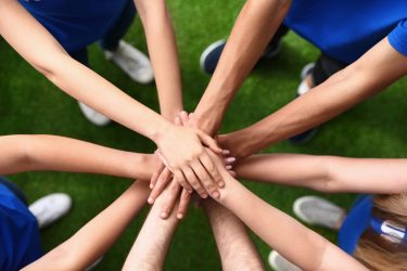 Group of volunteers joining hands together outdoors, top view