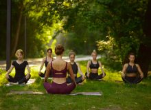 Women sits in yoga pose on the grass, group training. Meditation exercise, class on workout outdoors, relaxation practice